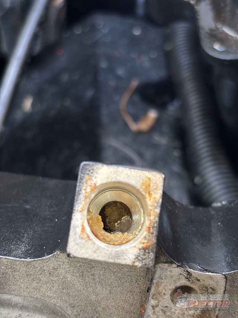 Fuel injector bore in a Mercruiser intake packed with hardened yellow-brown fuel varnish